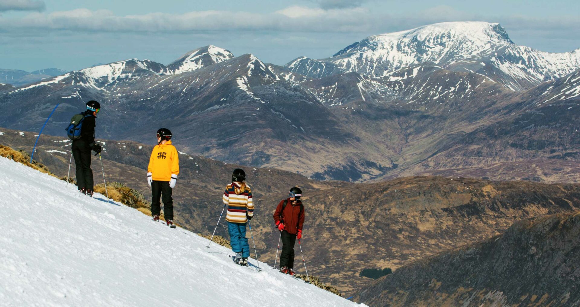 Four young people wearing ski wear are standing on snow covered Glencoe Mountain